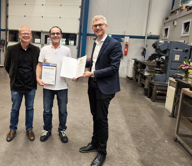 Bernhard Baumann (links) freut sich mit seinem langjährigen Mitarbeiter Juan Nieto (Bildmitte) über die Ehrenurkunde des Ministerpräsidenten, die Bürgermeister Michael Tauch zur Jubilarfeier überreicht hat.