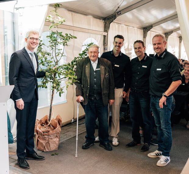 Bürgermeister Tauch (l.) überreicht ein Streuobstbäumchen als Jubiläumsgeschenk an (v.l.) Gerhard, Jan, Thomas und Wolfgang Schneider.